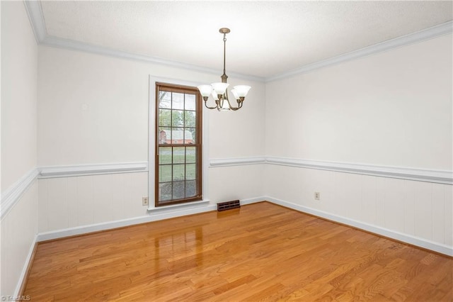 spare room with crown molding, wood finished floors, visible vents, and a chandelier