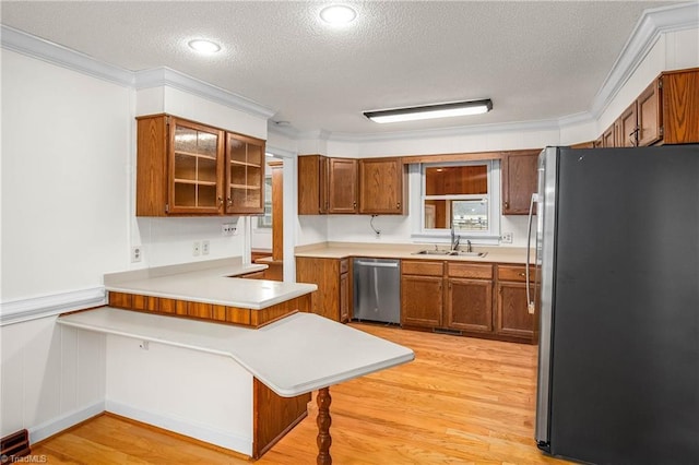 kitchen featuring crown molding, brown cabinets, a peninsula, light wood-style flooring, and stainless steel appliances