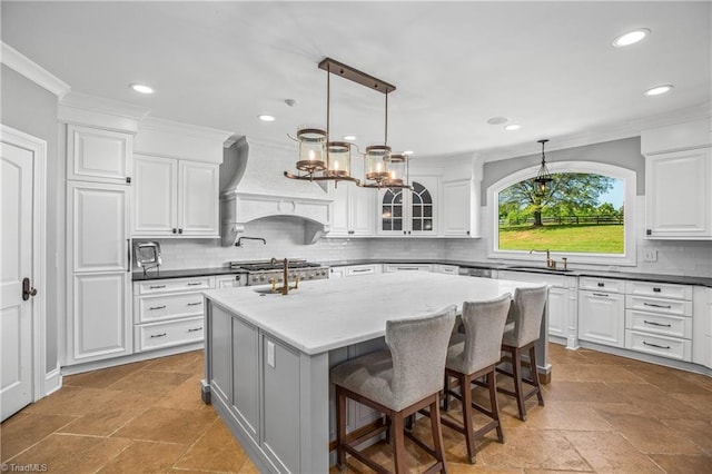 kitchen featuring hanging light fixtures, light tile flooring, custom range hood, a center island with sink, and a breakfast bar area