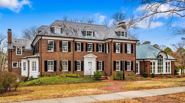 colonial home with a front yard, a standing seam roof, a high end roof, and brick siding