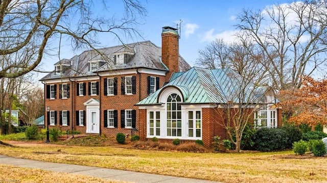 view of front of home with brick siding, a chimney, a front yard, a standing seam roof, and a high end roof