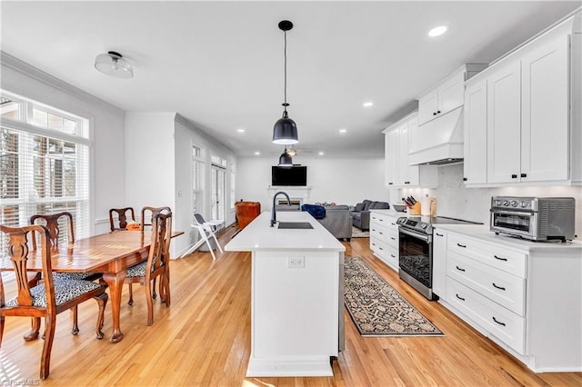 kitchen featuring sink, stainless steel electric range, an island with sink, decorative light fixtures, and custom exhaust hood