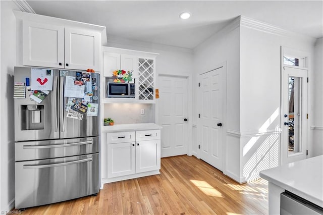 kitchen featuring white cabinetry, light wood-type flooring, ornamental molding, and appliances with stainless steel finishes