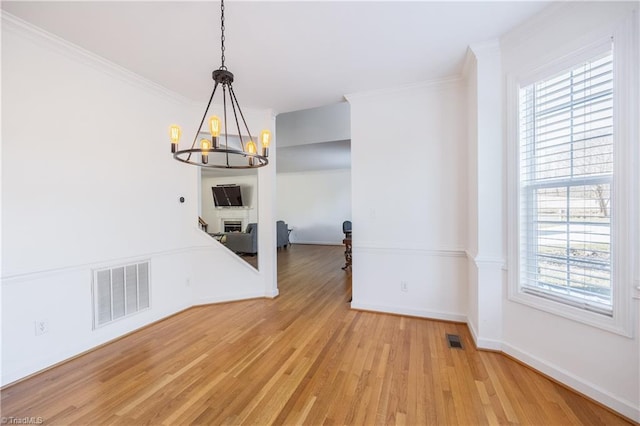 unfurnished dining area with a notable chandelier, crown molding, and light wood-type flooring