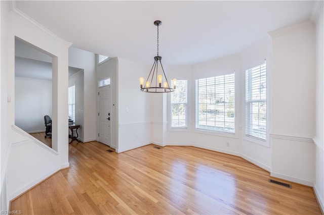 unfurnished dining area with ornamental molding, a notable chandelier, and light wood-type flooring