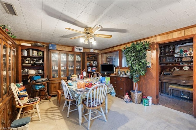 dining room with ornamental molding, wooden walls, and ceiling fan