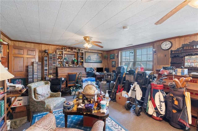 living room with wood walls, a wood stove, and ceiling fan