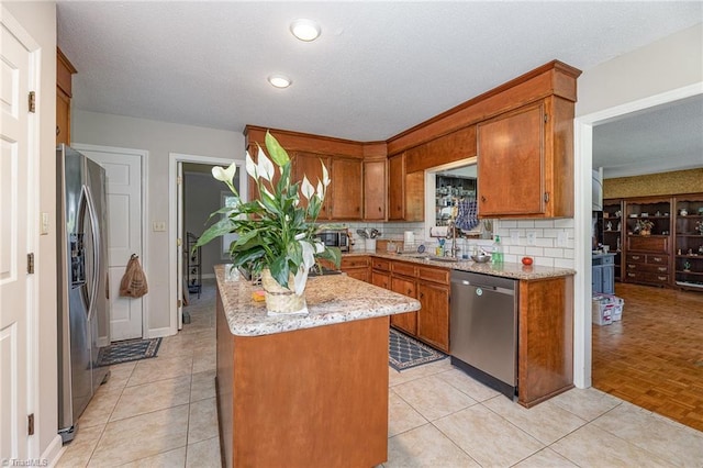 4680 Sherborne Dr, Pfafftown, NC 27040 - kitchen with appliances with stainless steel finishes, brown cabinetry, backsplash, light stone counters, and a textured ceiling