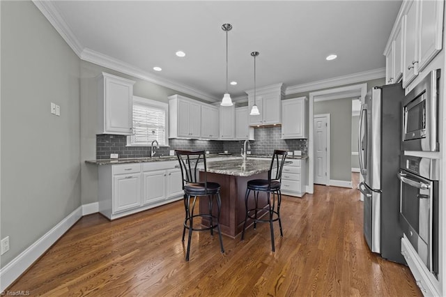 kitchen with a kitchen bar, decorative light fixtures, a center island, stainless steel appliances, and white cabinets