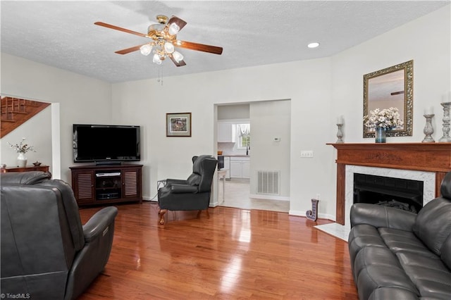 living room with hardwood / wood-style floors, ceiling fan, a premium fireplace, and a textured ceiling