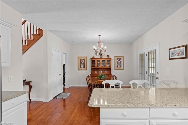 dining room with french doors, light hardwood / wood-style flooring, a textured ceiling, and a notable chandelier