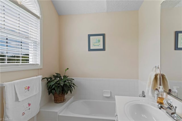 bathroom with a textured ceiling, vanity, and a bath