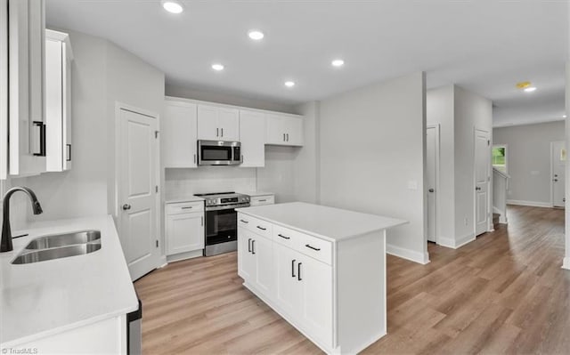 kitchen with appliances with stainless steel finishes, light wood-type flooring, a kitchen island, white cabinets, and sink