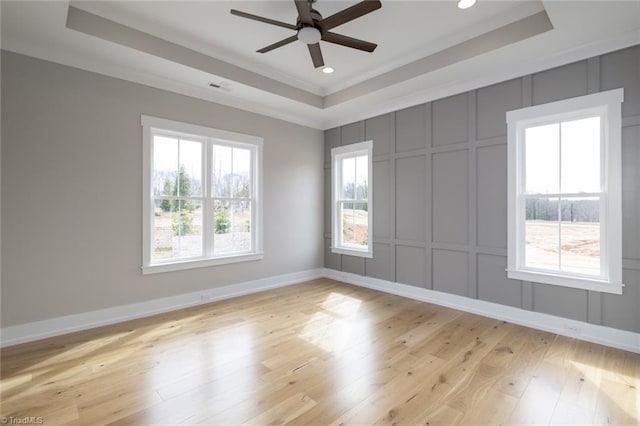 spare room with a tray ceiling, a decorative wall, ceiling fan, and light wood finished floors