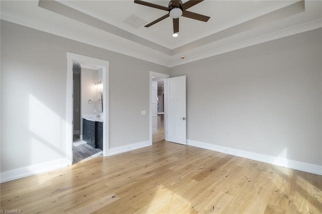 unfurnished bedroom with light wood finished floors, crown molding, a raised ceiling, and baseboards