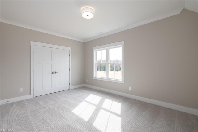 unfurnished bedroom with visible vents, baseboards, light colored carpet, ornamental molding, and a closet