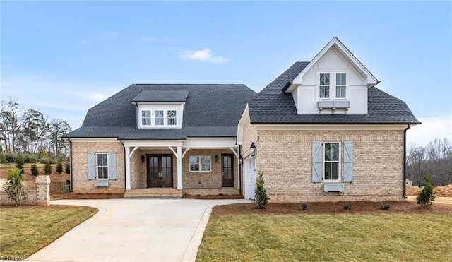 view of front of home with brick siding, a front lawn, roof with shingles, and driveway