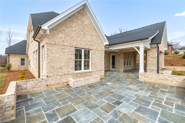 back of house with brick siding, roof with shingles, and a patio area