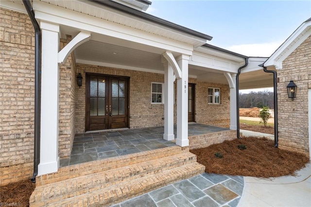 entrance to property featuring french doors, brick siding, and covered porch