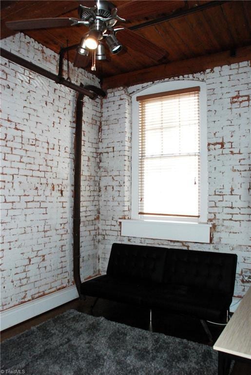 interior space featuring ceiling fan, brick wall, wooden ceiling, and baseboards