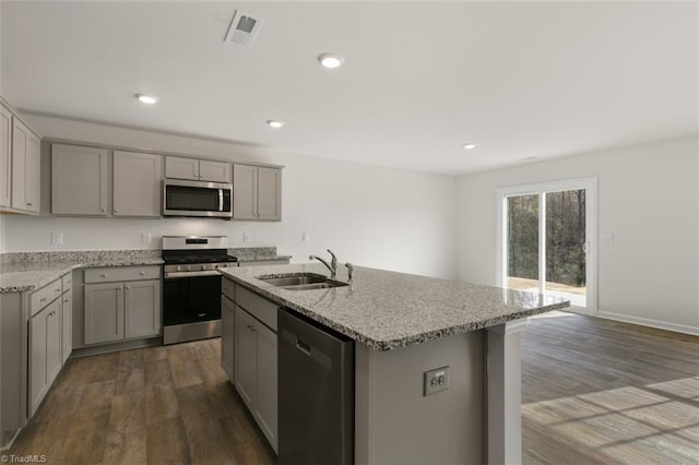 kitchen featuring light stone countertops, sink, wood-type flooring, a center island with sink, and appliances with stainless steel finishes