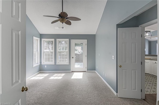 interior space featuring baseboards, carpet, ceiling fan, vaulted ceiling, and a textured ceiling