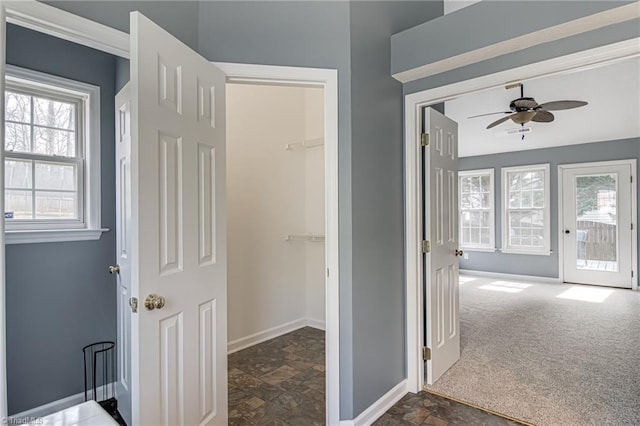 hallway with baseboards, dark carpet, and stone finish flooring