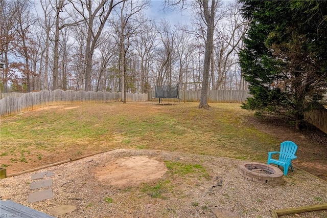 view of yard featuring a trampoline, a fire pit, and a fenced backyard