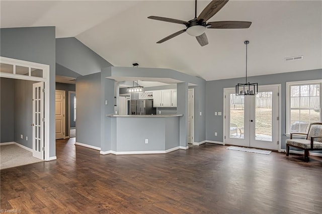 unfurnished living room featuring visible vents, vaulted ceiling, ceiling fan with notable chandelier, french doors, and dark wood-style floors