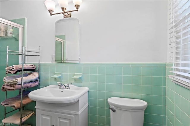 bathroom featuring vanity, toilet, a shower with shower door, and tile walls