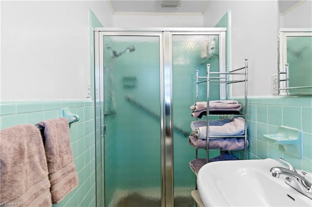 bathroom with crown molding, sink, a shower with shower door, and tile walls