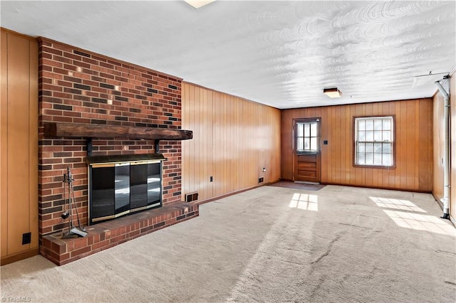 unfurnished living room with light carpet, wooden walls, and a brick fireplace