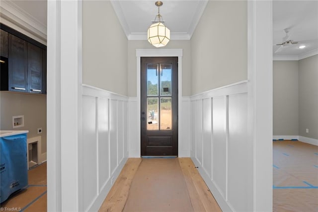 entryway with a ceiling fan, a wainscoted wall, light wood-style flooring, crown molding, and a decorative wall