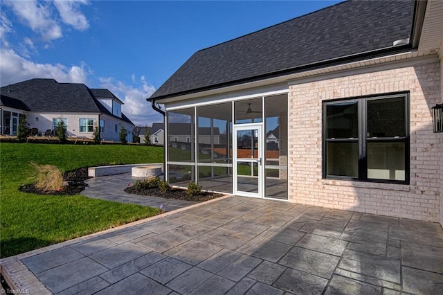 rear view of property with a sunroom, a shingled roof, a patio, and a yard