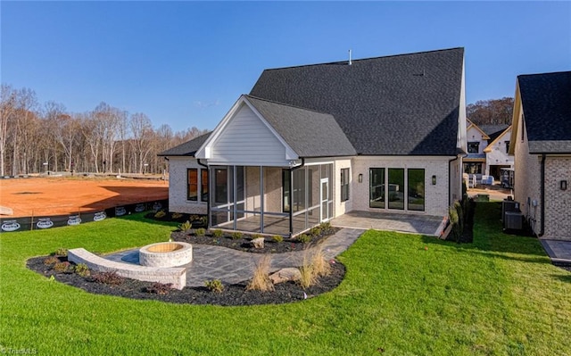 back of house with brick siding, a yard, a patio, an outdoor fire pit, and a sunroom