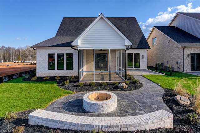 back of house with brick siding, a yard, a patio, a sunroom, and a fire pit