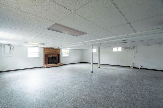 basement featuring brick wall, a brick fireplace, and a drop ceiling