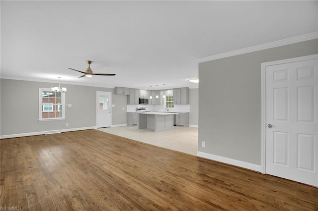 unfurnished living room featuring ornamental molding, ceiling fan with notable chandelier, and light hardwood / wood-style flooring