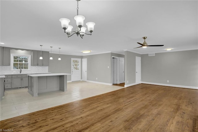 unfurnished living room with crown molding, ceiling fan with notable chandelier, and light hardwood / wood-style floors