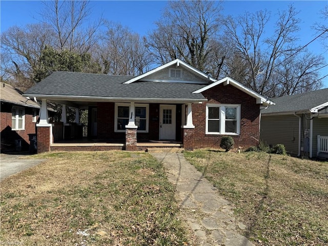 craftsman inspired home with a porch, a front yard, brick siding, and roof with shingles