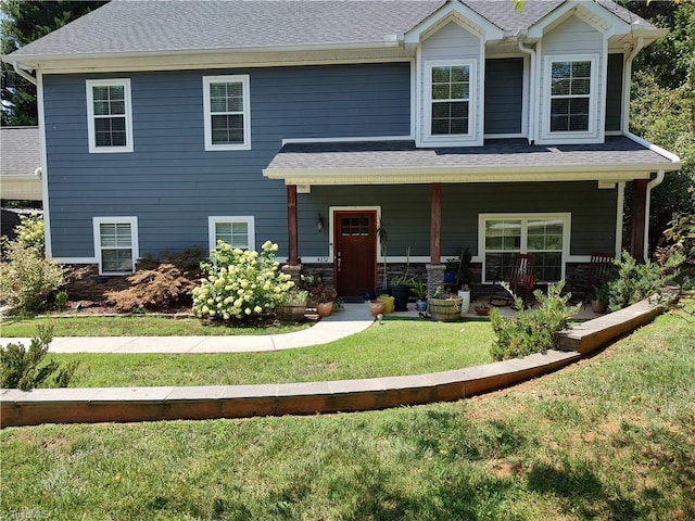 view of front of house with a shingled roof, stone siding, a porch, and a front lawn