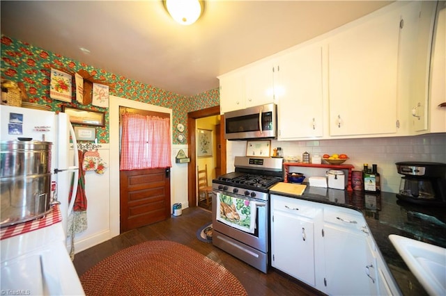 kitchen with decorative backsplash, dark stone countertops, dark wood-type flooring, white cabinets, and stainless steel appliances