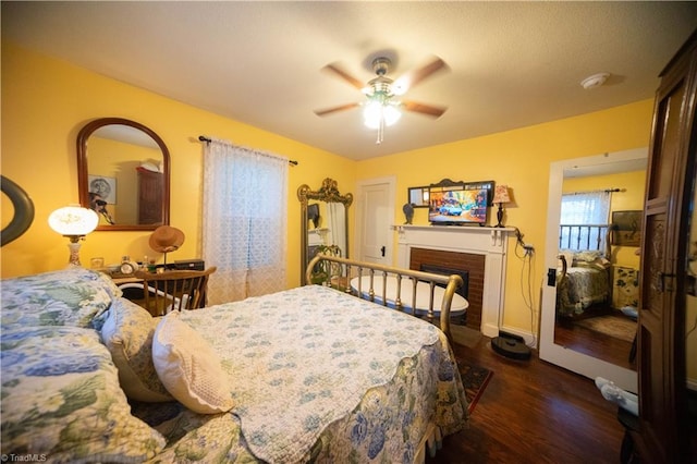 bedroom featuring a brick fireplace, dark hardwood / wood-style flooring, and ceiling fan