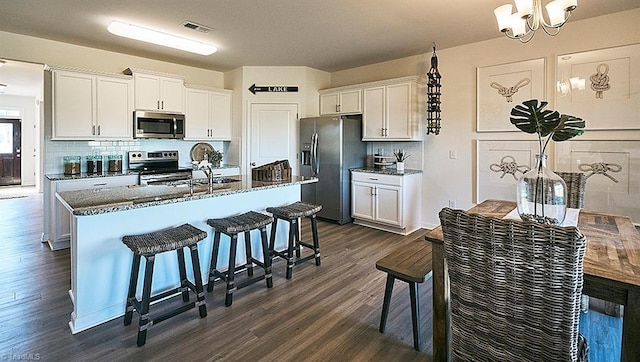 kitchen with hanging light fixtures, dark wood-type flooring, decorative backsplash, white cabinets, and appliances with stainless steel finishes