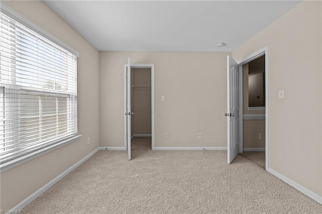 unfurnished bedroom featuring baseboards, a walk in closet, and light carpet