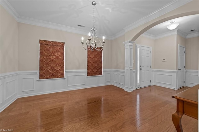 unfurnished dining area featuring decorative columns, arched walkways, visible vents, a notable chandelier, and wood finished floors