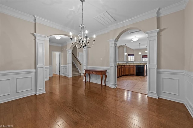 unfurnished dining area featuring decorative columns, a chandelier, wood finished floors, visible vents, and arched walkways