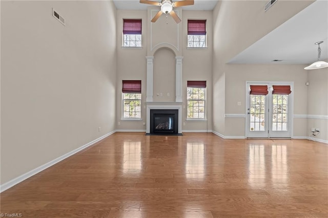 unfurnished living room featuring a ceiling fan, plenty of natural light, a fireplace with flush hearth, and wood finished floors