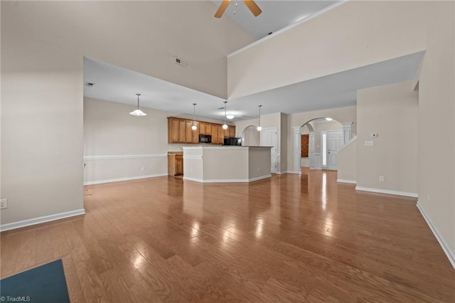 unfurnished living room featuring arched walkways, ceiling fan, baseboards, and light wood finished floors