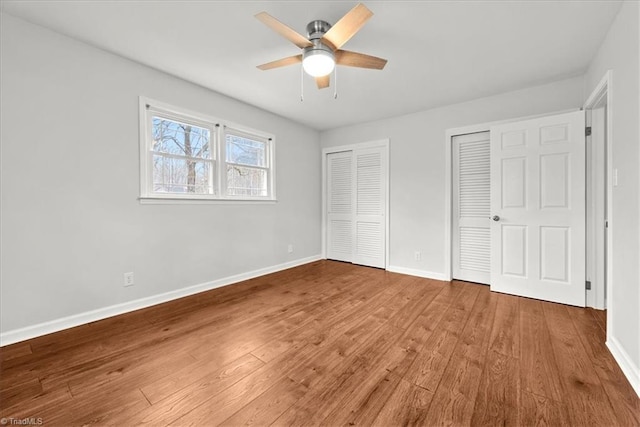 unfurnished bedroom with hardwood / wood-style floors, two closets, and ceiling fan